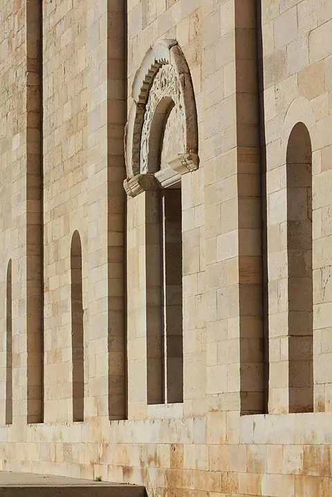 Un muro di pietra chiara a Trani, con arcate cieche e una finestra ad arco nella luce radente.