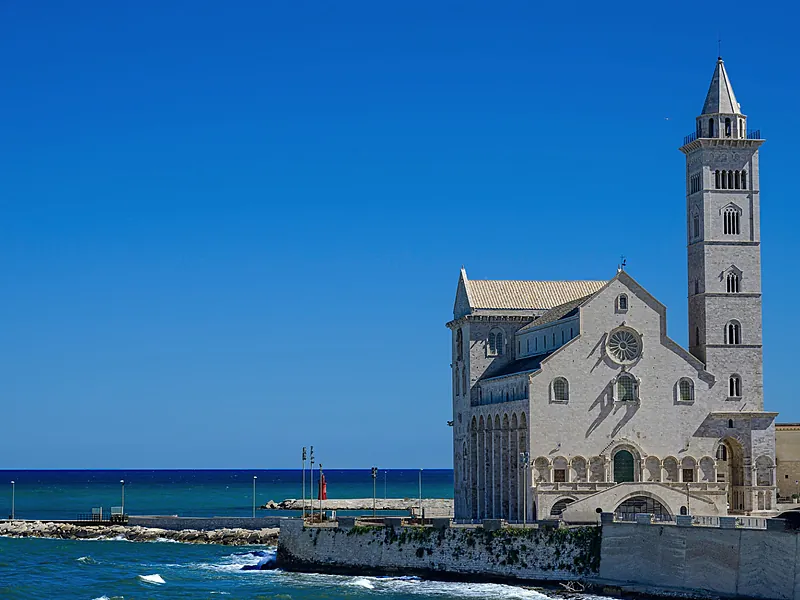 La cattedrale di Trani, in pietra chiara, affacciata sul mare sotto un cielo blu.