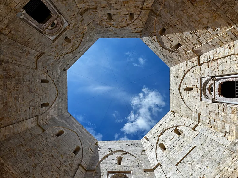Il cortile ottagonale di Castel del Monte visto dal basso, con il cielo azzurro e qualche nuvola.
