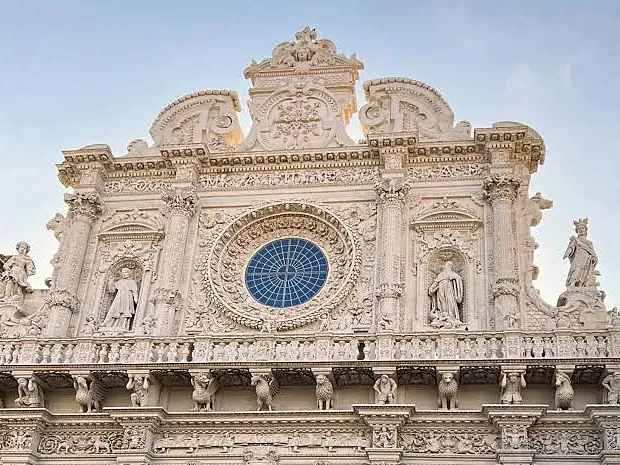 La facciata barocca di una chiesa di Lecce, con statue, colonne e un grande rosone.